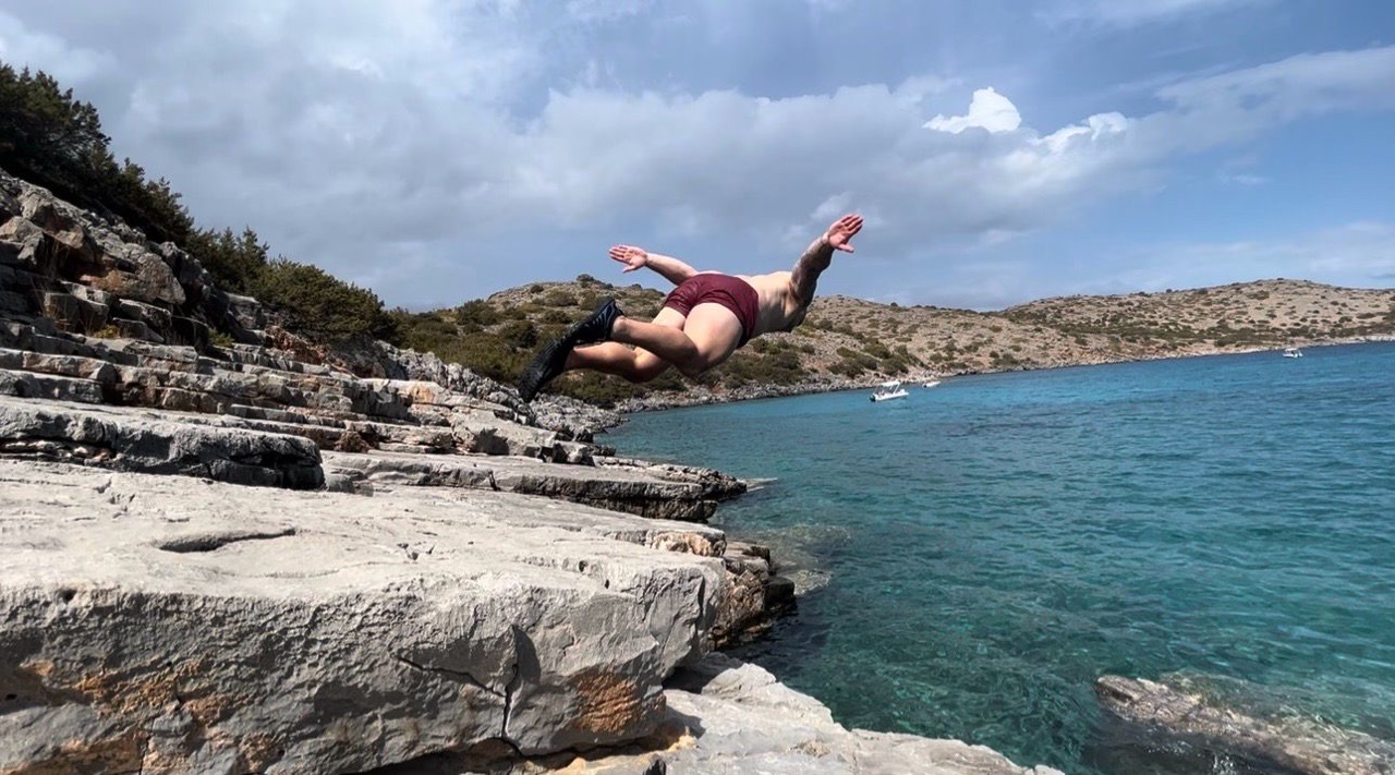 Craig Silkens diving from sunlit rocks into clear blue water